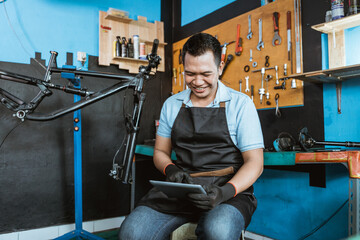 a bicycle mechanic sits using a digital tablet to browse during a break repairing a bicycle in a repair shop