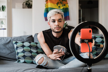 Gay man streaming online make up video tutorial with mobile phone indoors at home - Lgbt, drag queen, technology trendy concept - Focus in face