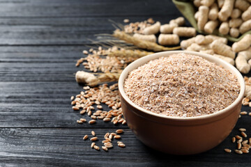Bowl of wheat bran on black wooden table, space for text