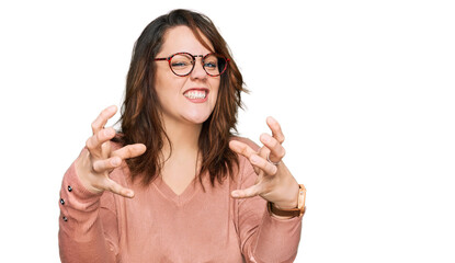 Young plus size woman wearing casual clothes and glasses shouting frustrated with rage, hands trying to strangle, yelling mad