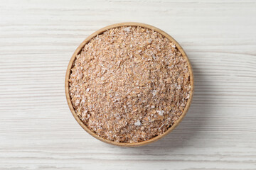 Bowl of wheat bran on white wooden table, top view