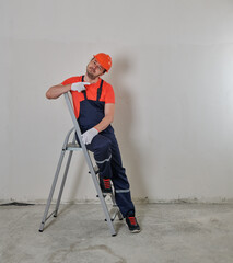 cheerful repairman sits on a stepladder in a helmet