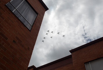 War airplanes in V formation flying over a residential unit with cloudy grey sky at background in colombian independence day