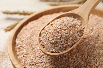 Spoon of wheat bran above bowl, closeup