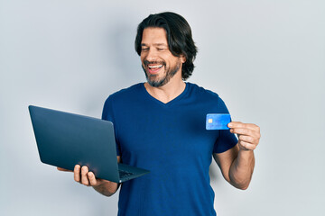 Middle age caucasian man wearing business style holding laptop and credit card smiling and laughing...