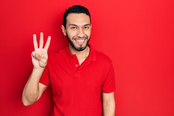 Naklejka premium Hispanic man with beard wearing casual red t shirt showing and pointing up with fingers number three while smiling confident and happy.