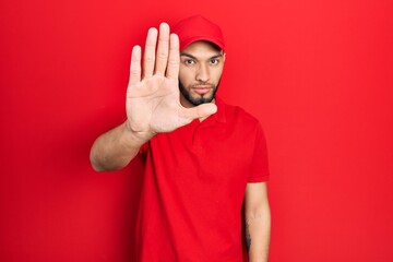 Hispanic man with beard wearing delivery uniform and cap doing stop sing with palm of the hand....