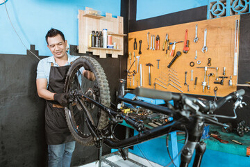 a bicycle mechanic in apron installs wheels when assembling a bicycle frame in a workshop