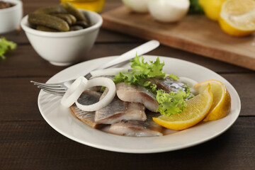 Sliced salted herring fillet served with lettuce, onion rings and lemon on wooden table