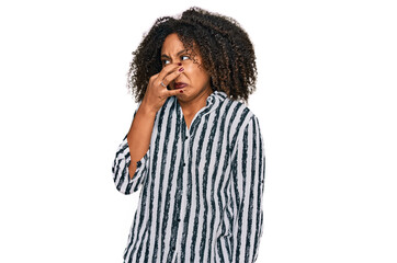 Young african american girl wearing casual clothes smelling something stinky and disgusting,...