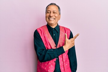 Middle age indian man wearing traditional indian clothes cheerful with a smile of face pointing...