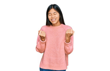 Beautiful young asian woman wearing casual winter sweater very happy and excited doing winner gesture with arms raised, smiling and screaming for success. celebration concept.
