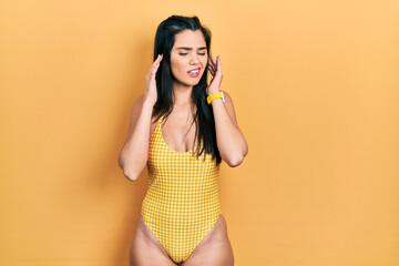 Young hispanic girl wearing swimsuit covering ears with fingers with annoyed expression for the noise of loud music. deaf concept.