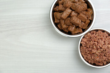 Different pet food in feeding bowls on white wooden background, flat lay. Space for text