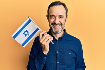 Middle age hispanic man holding israel flag looking positive and happy standing and smiling with a confident smile showing teeth