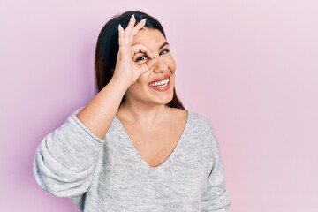 Young hispanic woman wearing casual clothes doing ok gesture with hand smiling, eye looking through fingers with happy face.