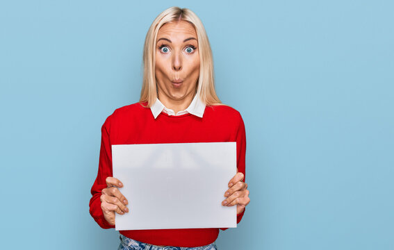 Young blonde woman holding blank empty banner scared and amazed with open mouth for surprise, disbelief face