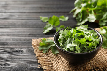 Cut fresh green cilantro in bowl on black wooden table. Space for text