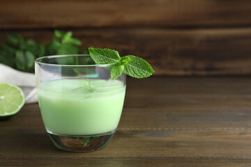 Delicious mint liqueur with green leaves on wooden table. Space for text
