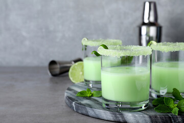 Delicious mint liqueur with ice cubes and green leaves on grey table. Space for text