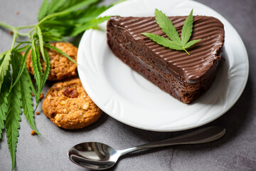 Chocolate cake and cookies with cannabis leaf - marijuana leaves plant on white plate on the wooden table, cannabis food nature herb concept