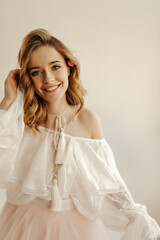 Cheerful lovely girl with curly blond hairstyle in white shirt with long sleeves looking into...