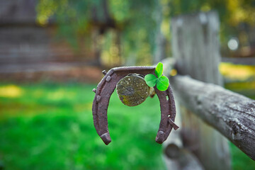 A rusty horseshoe and a leaf of clover hang on a wooden horse paddock.