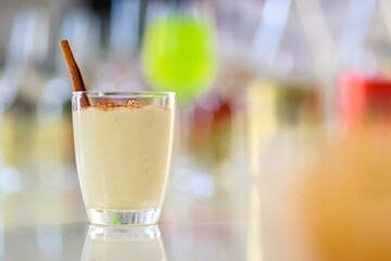 Tasty creamy spiced homemade eggnog drink with gingerbread in glass on middle of beverages table in Thanksgiving Christmas eve party surrounded by other alcoholic bottles liquor fries and snacks