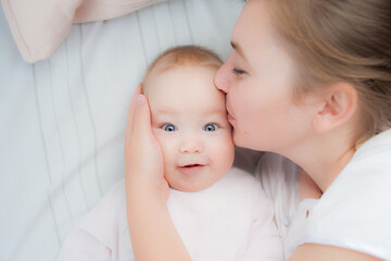 Happy mother kisses baby lying on the bed. Top view - 447606882