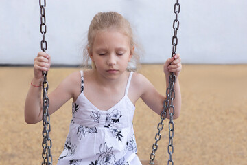 Sad and lonely child girl on a swing in the yard. Portrait middle plan