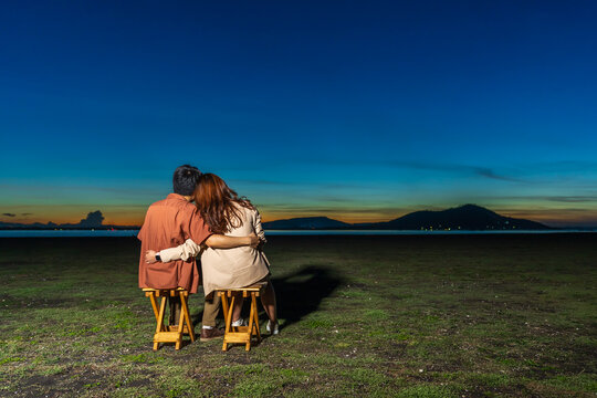 couple in love sitting and hugging at the grass filed at night