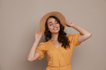 Beautiful young woman with straw hat on beige background