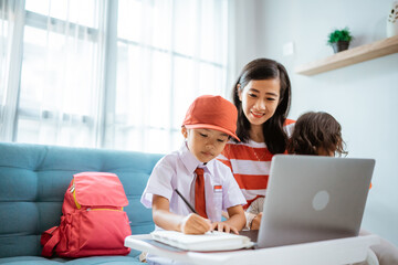 asian mother helping her daughter to study during online class meeting at home