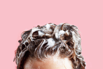 Fmale hair shampoo and foam on pink background close-up.