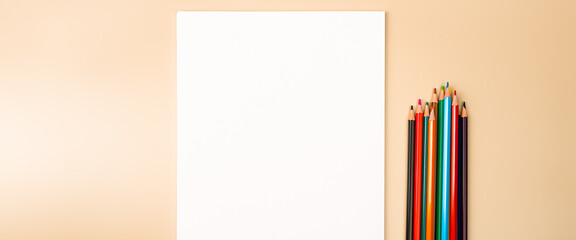 A blank white sheet and colored pencils for drawing on a plain textured background with space for copying and lettering.