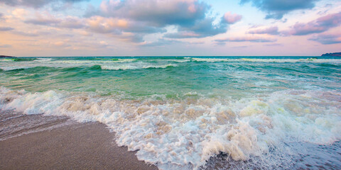 cloudy seascape scenery in evening light. waves crush on the sandy beach. dramatic weather nature background