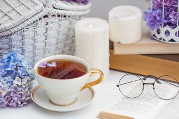 A visual for content. Still life in vintage style. A mug with a drink, an old book, a cage, candles and hydrangea flowers in the garden on a white wooden table. The concept of a tea ceremony.