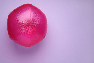 Bright beach ball on violet background, top view. Space for text
