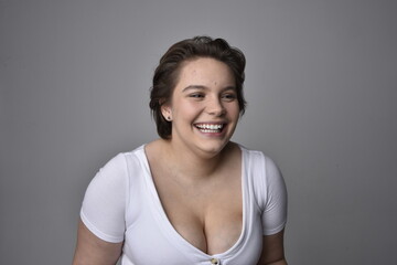 Close up portrait of young plus sized woman with short brunette hair,  wearing a white shirt, with over the top emotional facial expressions against a light studio background.  