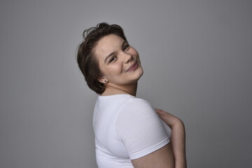 Close up portrait of young plus sized woman with short brunette hair,  wearing a white shirt, with over the top emotional facial expressions against a light studio background.  