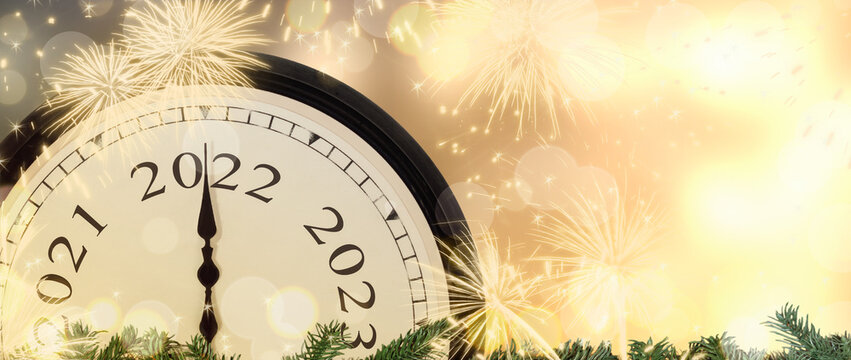 New Year's Eve 2022 concept. Clock pointer on year number 2022. Gold magic background with fireworks and blurred lights.