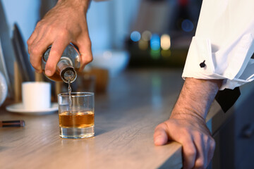 Senior man pouring drink into glass late in evening at home, closeup