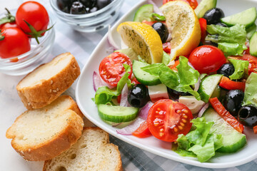 Plate with tasty Greek salad and bread on light background, closeup