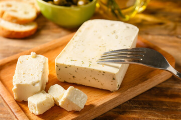 Board with tasty feta cheese on wooden background, closeup