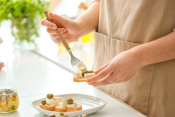 Woman making sandwiches with tasty feta cheese, oil and olives on light table in kitchen, closeup