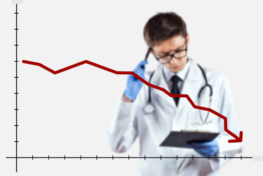 The doctor looks at the descending chart. The concept of reducing morbidity, vaccination and mortality. A man in a doctor's suit on a white background. - Powered by Adobe