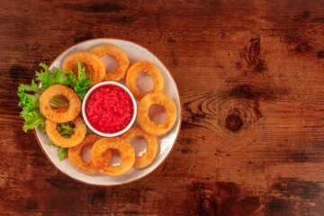 Squid rings. Deep fried calamari rings with lettuce and tomato sauce, shot from the top on a dark rustic wooden background with copy space