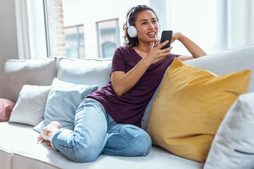 Smiling young woman listening to music with smartphone while sitting on sofa at home.