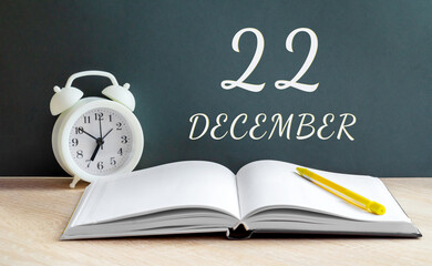 december 22. 22-th day of the month, calendar date.A white alarm clock, an open notebook with blank pages, and a yellow pencil lie on the table.Winter month, day of the year concept