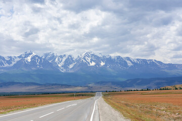 snowy peaks of mountains against the background of clouds and the road stretching into the distance